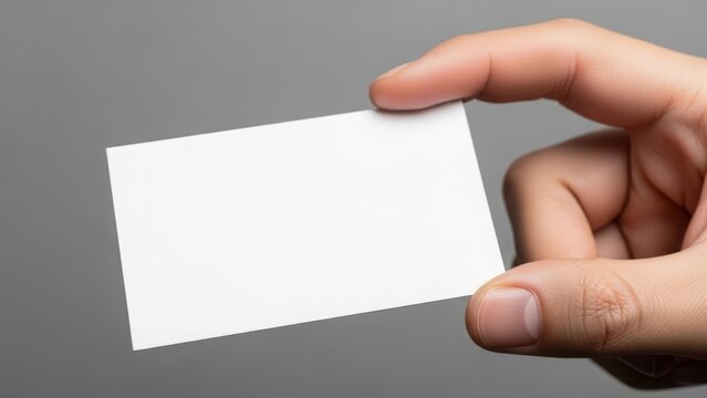 Hand holding a blank white business card against a plain gray background