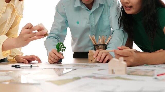 Architect and safety engineer discuss about position of tree use blueprint, model on table with architectural document, measurement tool and wooden block scatter around at modern office. Delineation.