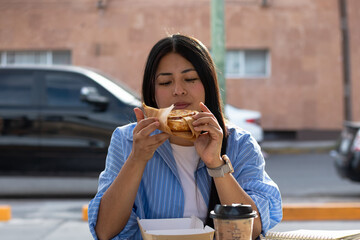 Young woman enjoying a delicious cinnamon roll and iced coffee, taking a relaxing break at an outdoor cafe, savoring the sweet pastry during a casual urban snack