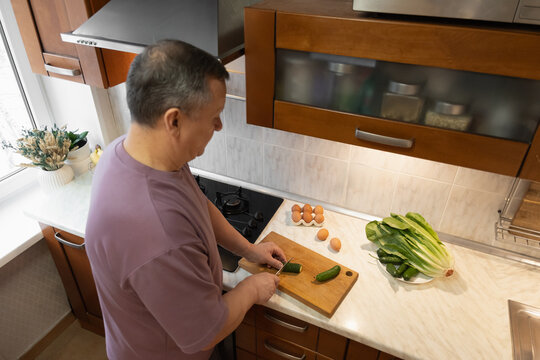 Man preparing healthy breakfast by slicing vegetables in home kitchen. Fresh ingredients and morning light. Morning Home Cooking Making and Eating Breakfast - Powered by Adobe