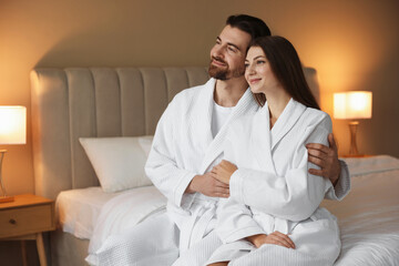 Fototapeta premium Happy couple in bathrobes on bed indoors. Space for text