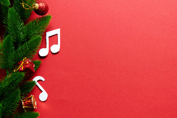 Festive arrangement featuring green pine branches, decorative ornaments, and musical notes on vibrant red background, creating a cheerful holiday atmosphere with copy space