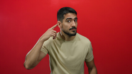 Young man posing against a vibrant red background showing various expressions looking thoughtful and welcoming in a casual beige shirt