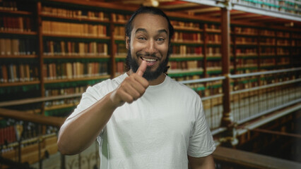 Man smiling, pointing finger at camera and giving thumbs up beside library bookshelves in a building  confidence. © Krakenimages.com