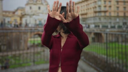 Young hispanic woman in red sweater holds palms out for denial outdoors at roman ruins building; rejection.