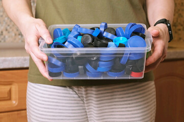 Woman holding clear plastic box packed with blue bottle caps in kitchen