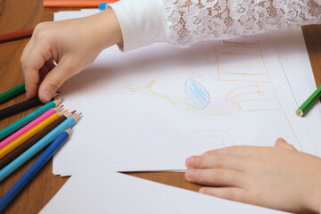 Childs hands reaching for colored pencil from bright row on wooden table