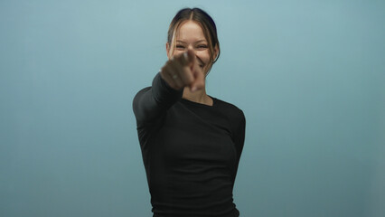 Woman pointing finger at camera in light blue studio with wide smiling expression; joy playfulness...