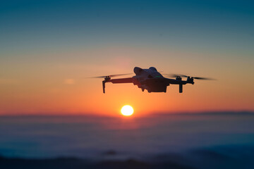 Drone flying hight in the sky. Orange sunset sun setting into  horizon in the background. Concept of aerial photography, technology and aviation.