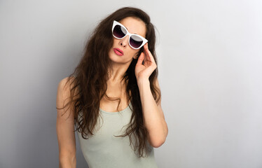 Portrait of elegant woman posing white sunglasses and fashion top on grey wall background with empty copy space for text. Front view face emotion sexy summer studio portrait