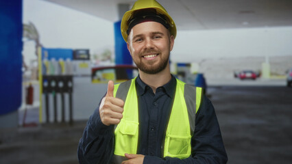 Man builder in yellow hardhat and fluorescent hi vis vest pointing and giving thumbs up at petrol station building  safety confidence. © Krakenimages.com