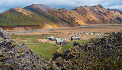 Iceland Travel - colorful scenic views of Landmannalaugar Fjallabak Nature Reserve base camp with lava rocks covered in moss in the foreground in summer.