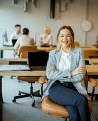 Business professional smiling in modern office setting with colleagues engaged in work