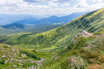 Naklejka premium Mountain valley landscape with green hills and distant blue peaks under cloudy summer sky