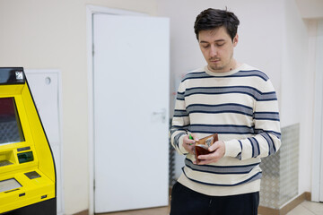 A young man at an ATM holding cash in his wallet