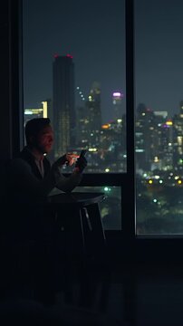 solitary man studies his phone screen with city lights reflecting on hotel window at night