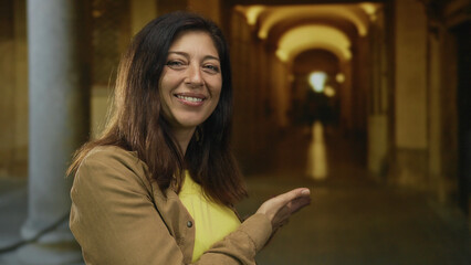 Woman standing outdoors pointing finger to historic university building corridor; curiosity discovery.