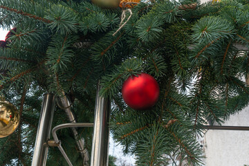Red Christmas ornament hanging on pine tree branch. Festive red bauble nestled among green pine needles in natural outdoor winter setting.