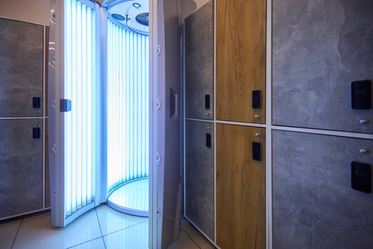 Spa treatment setup, Modern tanning room design features, Ultraviolet booth with wooden locker placement, Clinical style interior with blue UV lighting and tiled floor