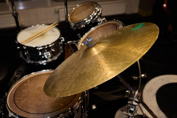 Closeup of shiny percussions, Intimate jazz club setting with textured metal and blurred audience, Glimmering cymbals and drums under warm amber light in cozy jazz venue