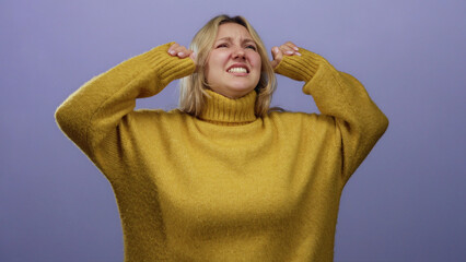 Woman covering ears in frustration against isolated purple background wearing mustard sweater...