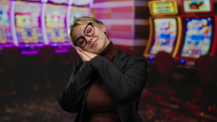Obraz premium Woman resting in casino with slot machines in the background, showing a relaxed posture amidst flashing lights and vibrant screens.