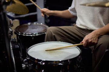 Drummer hands striking snare drum with sticks, captured midperformance showing motion blur, textured drumhead, casual stage clothing and focused groove driving live club energy