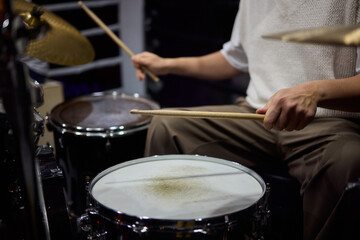 Drummer hands striking snare drum with sticks, captured midperformance showing motion blur, textured drumhead, casual stage clothing and focused groove driving live club energy
