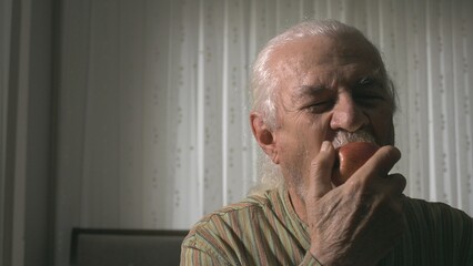 The man is seen biting into a bright red apple in his hand with great pleasure and appetite, and the sincere happiness and pleasure on his face are clearly visible.