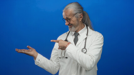 Man doctor points finger to open hand in studio against blue backdrop; health advice wellness confidence.