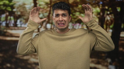 Man hands raise in outdoor scene as young hispanic fearful scared sweater guy reacts to sudden noise.