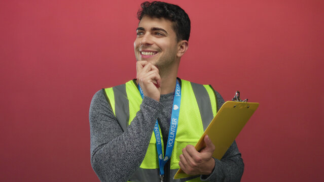 Man touches chin and seems to think against background colored wall while young hispanic volunteer grips clipboard beside guy.