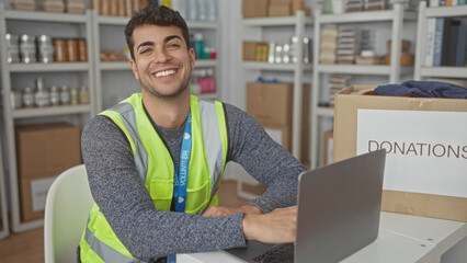 Man loads laptop for typing tasks at center computer station while hispanic young volunteer sorts donations for charity.