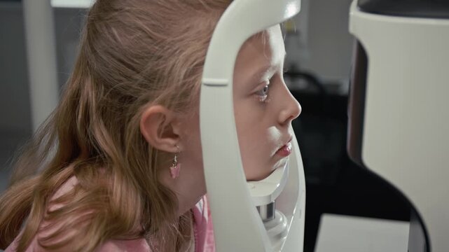 Side view close up shot of young girl looking into diagnostic machine and setting head in frame during eye exam in clinic, copy space