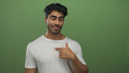 Young hispanic man wearing white t shirt with eyes closed and finger pointing to chest in green...