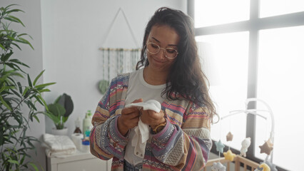 Woman holding a white baby onesie and smiling while inspecting the fabric in a nursery room inside...