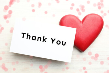 Thank You card and red decorative heart on white wooden table, top view