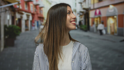 Fototapeta premium Woman smiling with hair down and wearing striped shirt on street lined with city buildings; happiness.