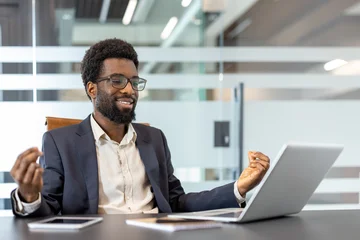Fotobehang Lotusbloem Young businessman meditating in lotus position while sitting at desk inside office. Man browsing online meditation training courses using laptop.  © Liubomir