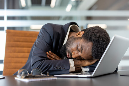African american businessman asleep at his desk with laptop and glasses, exhausted and overworked, illustrating workplace burnout, chronic fatigue and stress in a corporate office setting - Powered by Adobe