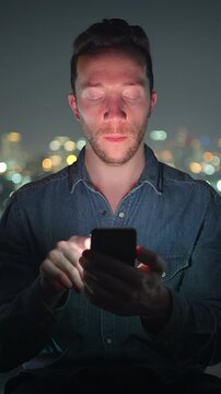 individual engrossed in digital display, person gazing at phone screen with city lights blurred background