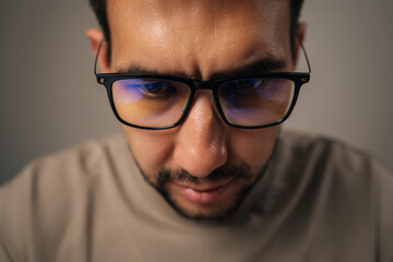 Close-up portrait of focused employee male working on laptop computer, wearing blue light-filtering glasses to shield eyes from screen glare in professional setting. Concept of remote workplace.