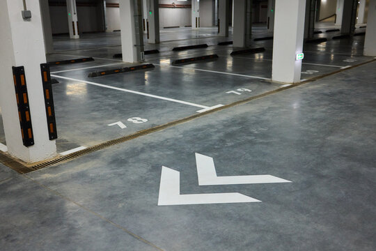 Brightly marked vehicle storage area, Concrete structure with guiding arrows and lighting, Industrial style subterranean garage with safety features and signage present