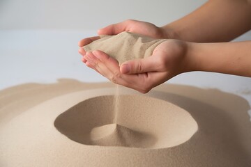 Delicate Balance: Hands Holding Sand Above a Meticulously Formed Sandscape, Highlighting the Ephemeral Nature of Existence.