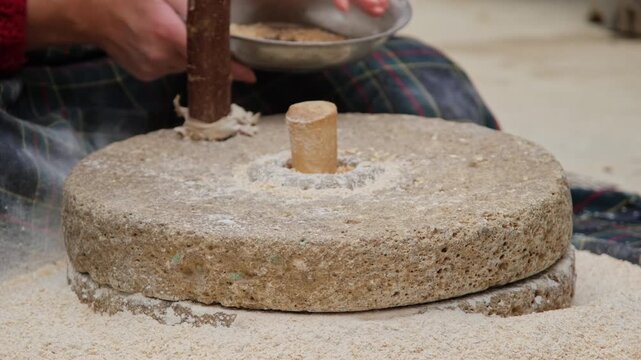 Woman grinding wheat grains with traditional hand millstone