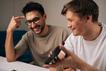 Positive young men in office collaborating on startup plan, using smartphone for calls and messages, sharing ideas, planning strategy and driving innovation and growth.