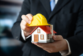 A man puts a yellow construction helmet on a house. House renovation. Building reconstruction. Structural repair modernization. Construction industry updates, property maintenance, home improvement.