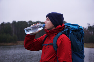 A male tourist with a hiking backpack drinking water from a bottle. Hiker quenches his thirst while resting on a hike