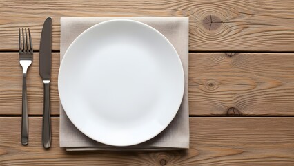 Empty white dinner plate setting with stainless steel fork and knife placed neatly on neutral napkin over rustic wooden table