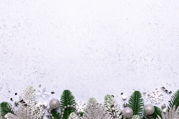 Festive Christmas border with fir tree branches and silver decorations on light marble background top view, copy space for your design.